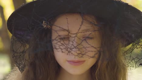 Close-up-of-a-redhead-Caucasian-girl-in-Halloween-witch-hat-standing-in-the-autumn-park.