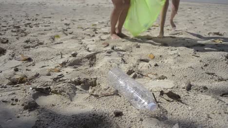 Mom-and-her-daughter-collecting-garbage-on-the-sandy-beach-into-green-plastic-bag,-Plastic-bottles-are-collected-on-the-beach,-Volunteers-cleaning-the-beach.