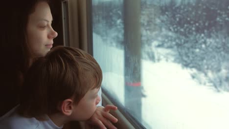 Mutter-und-Sohn-schauen-in-senin-Fenster-in-bewegenden-Zug-auf-Winterlandschaft.