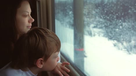 Mom-and-son-are-looking-in-window-in-moving-train-on-winter-landscape.