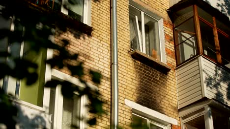 Through-the-foliage-of-trees-we-see-a-wall-with-windows-and-balconies