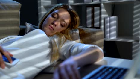 Müde-Geschäftsfrau-schlafend-auf-der-Couch-im-Büro-mit-Laptop-und-Telefon