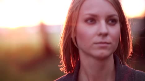 Portrait-of-young-pensive-woman-at-the-park,-looking-into-the-distance-in-the-rays-of-the-setting-sun,-close-up