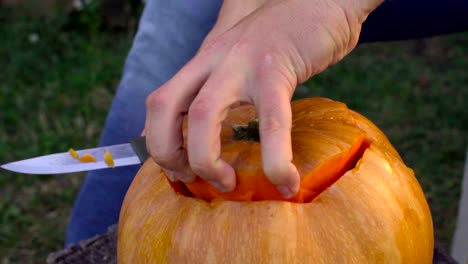 Man-carves-from-a-pumpkin-Jack-o'-lantern-in-the-backyard-on-a-tree-stump