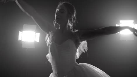 Professional-ballerina-dancing-ballet-in-spotlights-on-big-stage.-Beautiful-caucasian-young-girl-wearing-white-tutu-dress.-Black-and-white-vintage-retro-effect-tonned.-4k