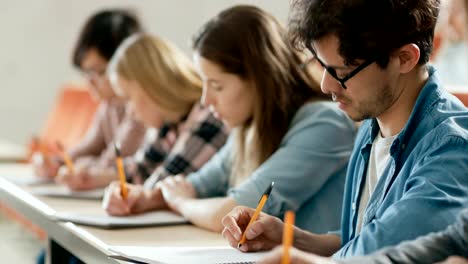 Reihe-von-Multi-ethnischen-Schülern-in-der-Klasse-die-Prüfung-/-Test-/-schreiben-in-Notebooks.-Helle-Jugendliche-Studie-an-der-Universität.