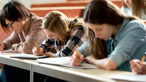 Fila-de-Multi-étnica-de-estudiantes-en-el-aula-de-examen-/-prueba-/-escribir-en-cuadernos.-Luminoso-estudio-en-la-Universidad-de-los-jóvenes.