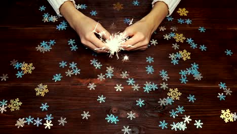 Female-hands-holding-a-burning-sparkler-over-wooden-table-with-decorations