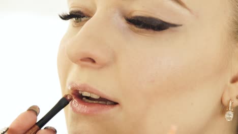 Hand-makeup-artist-with-cosmetic-brush-painting-lips-on-woman-face.-Makeup-lips-close-up