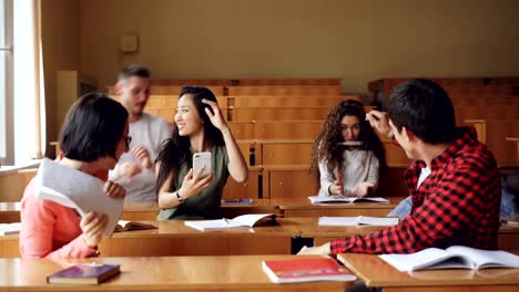 Carefree-students-are-having-fun-after-lecture-throwing-paper,-drawing-in-notebooks,-fighting-and-laughing.-Naughty-youth,-education-and-relaxation-concept.