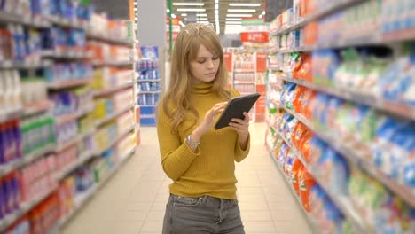 Joven-mujer-de-compras-en-el-hipermercado-y-buscando-información-sobre-los-productos-en-su-tablet