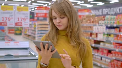 Women-shopping-at-the-supermarket-and-using-mobile-apps-on-her-tablet