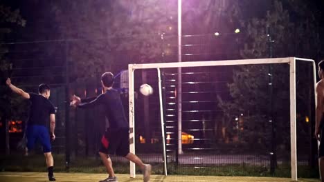 Hombre-joven-Patea-una-pelota-que-vuela-más-allá-de-otros-jugadores-de-fútbol-y-más-allá-de-la-puerta,-juego-de-Futbol-tiro-de-noche