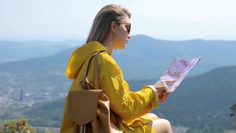 Hiker-in-a-yellow-raincoat-looking-at-map-from-mountain-top.-woman-with-map-in-mountains-FullHD