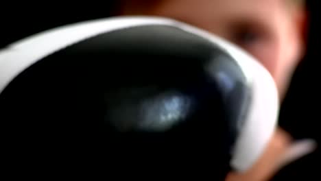 The-young-boxer-stands-on-a-dark-background.-In-the-foreground-is-his-black-and-white-glove,-his-face-is-partially-visible,-it-is-blurry