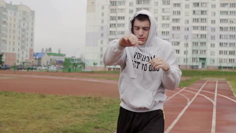 Junger-Mann-Training-im-Hoodie-Boxen-mit-unsichtbaren-Gegner-im-Stadion.