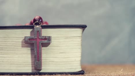 Open-Bible-and-the-crucifix-beads-on-a-golden-table,-close-up.-Beautiful-dark-background.-Religion-concept