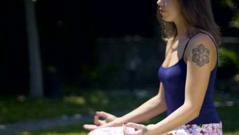 Beautiful-woman-with-tattoos-sits-in-lotus-pose-deeply-meditating-outdoors-park