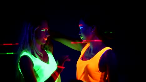 Women-with-UV-face-paint,-laser,-glowing-bracelets,-glowing-clothing-dancing-together-in-front-of-camera,-Half-body-shot.-Caucasian-and-asian-woman.-.