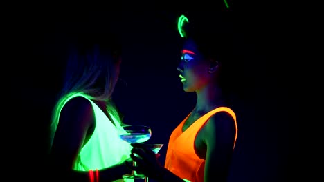 Women-with-UV-face-paint,-laser,-glowing-bracelets,-drinks,-glowing-clothing-dancing-together-in-front-of-camera,-Half-body-shot.-Caucasian-and-asian-woman.-.