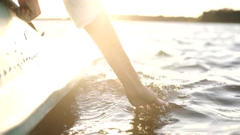 En-primer-plano-al-atardecer,-la-mano-de-una-chica-pasando-por-el-agua