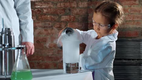 Child-scientist-pouring-liquid-nitrogen-from-steel-thermos-bottle-in-beaker