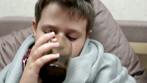 The-boy-drinks-medicine-and-tea-with-lemon.-He's-got-a-cold