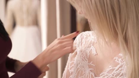 A-close-up-of-designer's-hands-taking-pins-away-from-the-fabric-on-the-shoulder-seam-and-showing-the-lines-on-the-veiling-embroidered-fancy-dress-to-her-client.-The-camera-moves-top-down