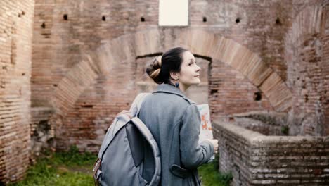 Back-view-of-excited-young-female-student-researcher-with-backpack-and-map-exploring-ancient-ruins-in-Ostia,-Italy.