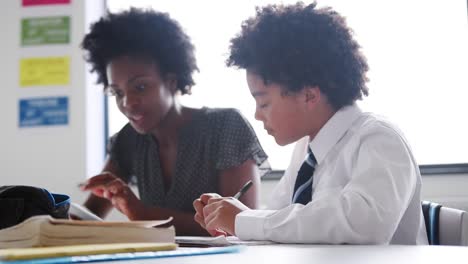 Tutor-de-secundaria-mujer-con-tableta-Digital-dando-estudiante-masculino-con-uniforme-enseñanza-uno-a-uno-en-el-escritorio