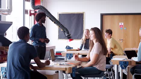 Lehrer-im-Gespräch-mit-der-Gruppe-von-Schülerinnen-und-Schüler-sitzen-an-Werkbänken-In-Design-und-Technologie-Lektion