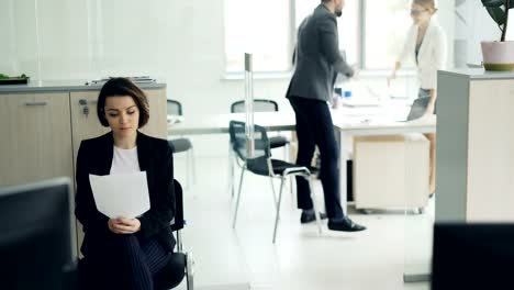 Joven-atractivo-está-esperando-en-la-oficina-leyendo-su-currículum,-mientras-que-otro-candidato-está-hablando-con-el-entrevistador-entonces-chica-es-entrar-en-sala-y-Gerente-de-saludo.