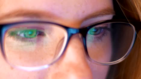 Close-up-reflection-of-laptop-screen-in-gleasses-of-caucaisna-girl-hacker,-looking-at-copmuter,-beautiful-eyes-of-smart-person-indoor