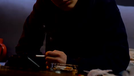 Man-lighting-cigarette-and-smoking-it,-table-with-ashtray-cup-and-joystick