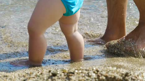 Im-Urlaub-Eine-Mama-macht-die-ersten-Schritte-zu-seinem-kleinen-Baby-am-Strand-Schritt-für-Schritt-lernt-das-Neugeborene-zu-gehen-...