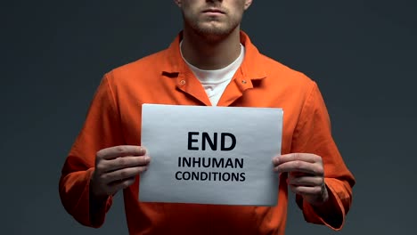 End-inhuman-conditions-phrase-on-card-in-hands-of-Caucasian-prisoner,-protest