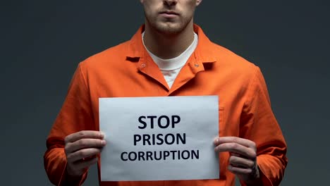 Stop-prison-corruption-phrase-on-cardboard-in-hands-of-Caucasian-prisoner