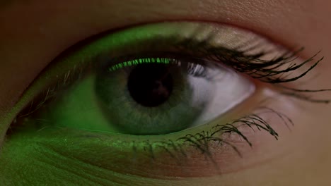 Close-up-shoot-of-light-blue-eye-blinking-with-reflection-of-lamp-on-it-in-green-light.