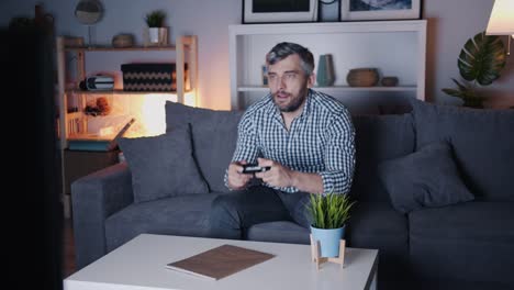 Bearded-guy-enjoying-video-game-at-home-at-night-on-sofa-holding-joystick