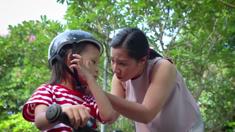 Mother-helping-her-son-(Long-hair-boy)--to-put-on-bicycle-helmet-outdoors.