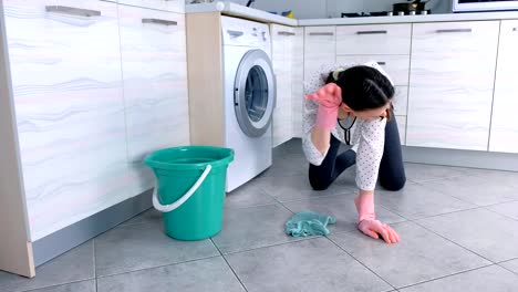 Tired-woman-in-pink-rubber-gloves-washes-the-kitchen-floor-with-a-cloth.-Gray-tiles-on-the-floor.