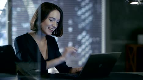 Female-Executive-Works-on-a-Laptop-in-Her-Private-Office-with-Big-City-View.-She's-Laughing-Charmingly.-Her-Workspace-is-Done-in-Dark-Overtones.