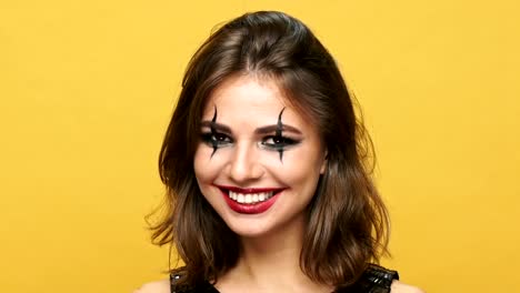 Happy-cheerful-lady-with-dark-make-up-and-right-red-lipstick-smiling-amd-showing-thumbs-up-isolated-over-yellow-background