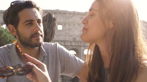 Turistas-de-la-feliz-pareja-jóvenes-sentados-en-el-bar-restaurante-frente-Coliseo-en-Roma,-en-la-puesta-de-sol-charlando-y-riendo