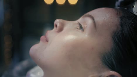 Hairdresser-in-black-professional-gloves-washes-the-woman's-long-dark-hair-in-sink-in-beauty-salon.-Closeup