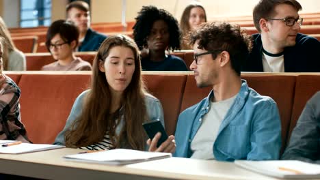 Estudiante-masculino-acciones-pantalla-de-teléfono-móvil-con-estudiante-del-compañero-durante-la-Conferencia.-Uso-de-medios-sociales-en-las-aulas-universitarias.