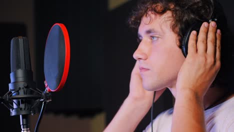 Young-handsome-singer-man-puts-on-headphones-in-the-studio.-Recording-new-melody-or-album.-Male-vocal-artist-with-curly-hair-preparing-for-working.-4k