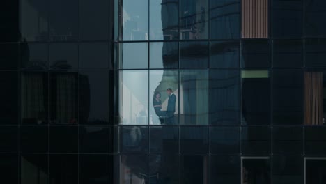 Aerial-Footage-From-Outside:--Businessman-and-Businesswoman-Talking-Business-while-Standing-next-to-Skyscraper-Office-Window.-Flying-Shot-of-the-Financial-Business-District-of-the-Big-City.