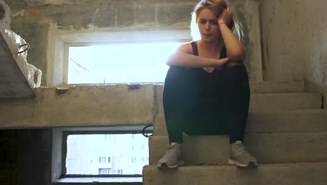 Young-unhappy-girl-is-sitting-at-the-stairs-in-an-abandoned-building