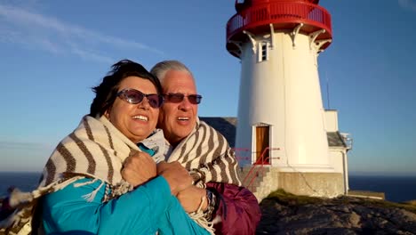 A-Mature-couple-admires-the-sunset-on-the-sea-coast-with-an-old-lighthouse.